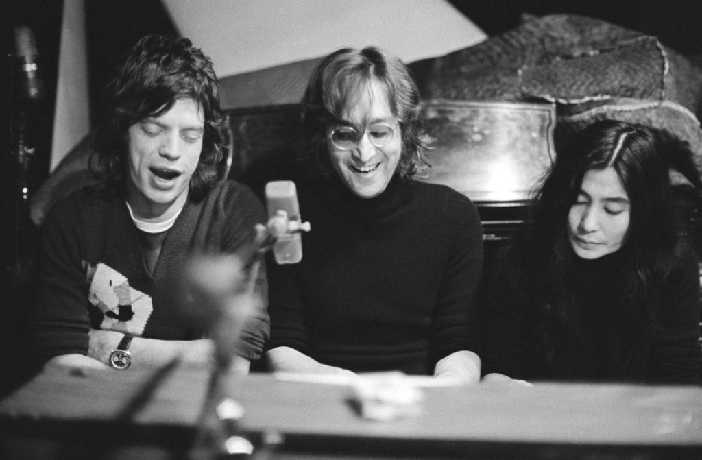 (L-R) Mick Jagger of The Rolling Stones, John Lennon and Yoko Ono singing at a piano at The Record Plant, NYC. October 1972.  Copyrights to Bob Gruen © All Rights Reserved.Lens Magazine
