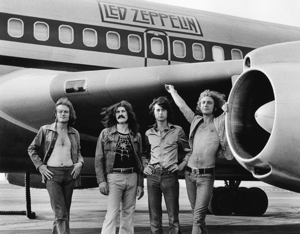(L-R) John Paul Jones, John Bonham, Jimmy Page and Robert Plant of Led Zeppelin in front of plane in NY. July 24, 1973. Copyrights to Bob Gruen © All Rights Reserved. Lens Magazine
