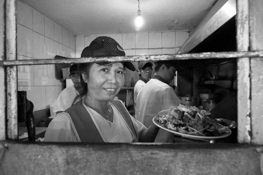 Laura Chi, Chinese born of Chinese father and Mexican mother, at the kitchen of her Chinese restaurant.
ISO 6400, 1/125, f/5.6, 24 mm, aperture priority.
Sony a99, Zeiss Vario-Sonnar 24-70 mm F2.8. Software: Capture One 10
Carlos Paz-Bordone © All rights reserved.
