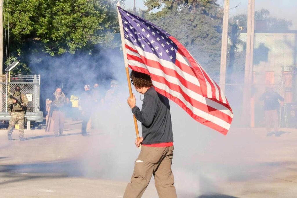 Broadview’s Stand #7
A Veteran waves an American flag at federal agents as they fire tear gas and pepper pellets at the protesters at the side entrance of the ICE detention facility on 25th street and Harvard in Broadview, IL, USA. Since early September, protesters have returned to this facility to attempt to block operations tied to enforcement sweeps.
Alexandra Buxbaum © All rights reserved.