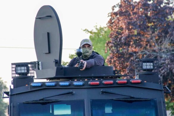 Right Page Top: Broadview’s Stand #3 A federal agent points a weapon as a few armed Federal agents come to remove the posters put up on the front of the security fencing surrounding the front entrance of the ICE detention facility on Beach Street in Broadview, IL, USA. Since early September, protesters have returned to this facility to attempt to block operations tied to enforcement sweeps. Alexandra Buxbaum © All rights reserved.