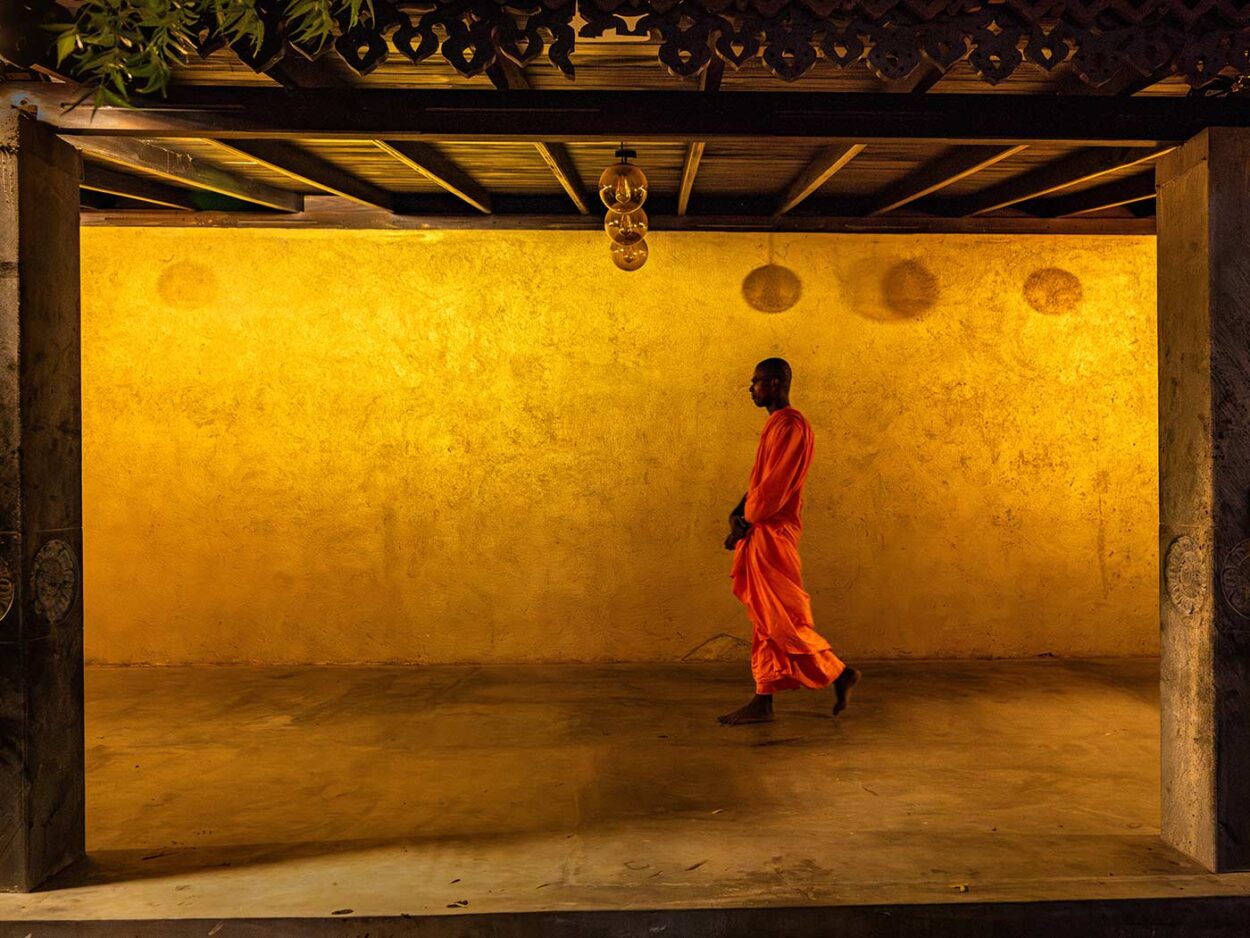The Saffron Walk A Buddhist monk walks through a temple corridor in Kataragama, in Sri Lanka, his saffron robe standing out against the warm interior light. The image reflects the quiet discipline of monastic life, structured by movement, prayer, and daily ritual. Thibault Gerbaldi © All rights reserved
